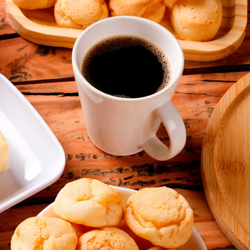 A cup of black coffee accompanied by homemade cheese bread, served in a natural fiber basket on a rustic wooden table.