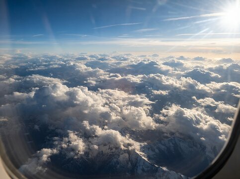 View from airplane window above fluffy white clouds at sunset.