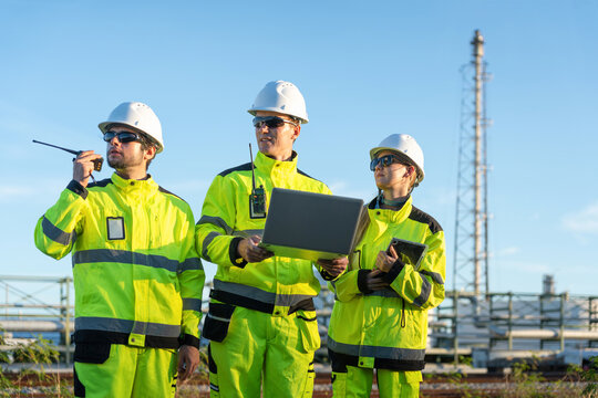oil refinery engineers with laptop and walkie talkie at plant, petroleum plant team working together with technology outdoors, energy industry professionals inspecting industrial facility site