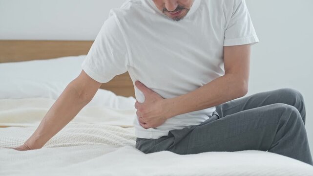 Senior man suffering from lower back pain. Acute lower back strain, middle-aged/older adult, aging, pain, trouble, herniated disc, bed, health.