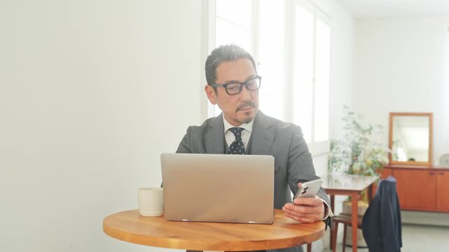 スマホとノートPCを使うミドル男性。DX、スマホ、パソコン、認証、通販、動画、SNS、金融、仕事