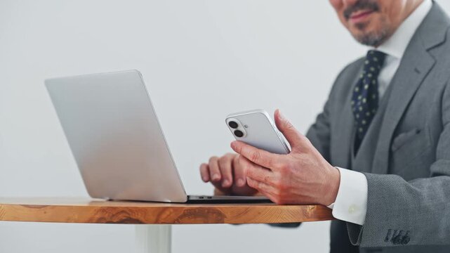 Middle-aged man using a smartphone and laptop. DX, smartphone, PC, authentication, online shopping, video, social media, finance, work.