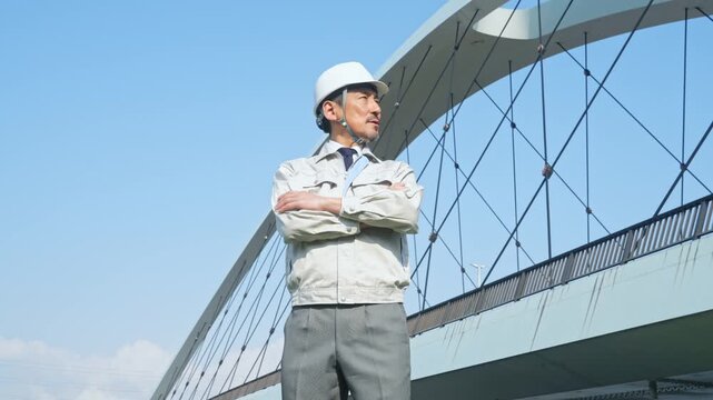 橋の前で遠くを眺める男性作業員。建設、工事、インフラ、点検、検査、メンテナンス、保守、安全、修理