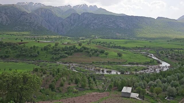 A solitary house stands amid orchard rows on a hilltop, overlooking a winding river valley beneath snow-capped peaks and a dramatic sunlit sky
📍 Marivan, Kurdistan, Iran 