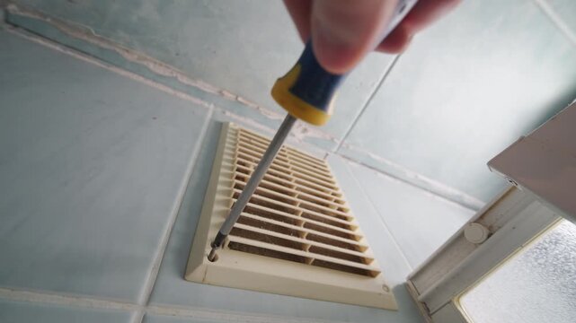 Ultra Wide-Angle Bottom View: Repairman Unscrewing Bathroom Ventilation Grille Screw | Hand Holding Screwdriver Fixing Air Vent Cover | Home Maintenance Repair Close-Up