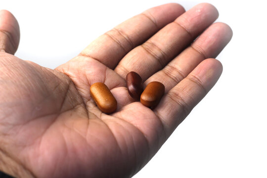 An open human hand holding three smooth brown oval supplement pills against a white background