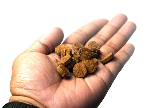 open palm filled with a small pile of round, rough-textured brown herbal tablets isolated on a white background.