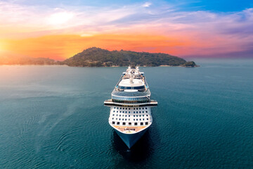 Obraz premium Aerial straight view typical cruise ship sailing on the ocean during a golden summer sunset with islands and mountains in the background.