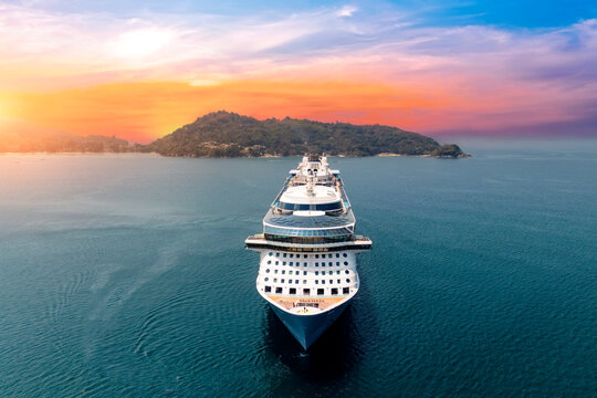 Aerial straight view typical cruise ship sailing on the ocean during a golden summer sunset with islands and mountains in the background.