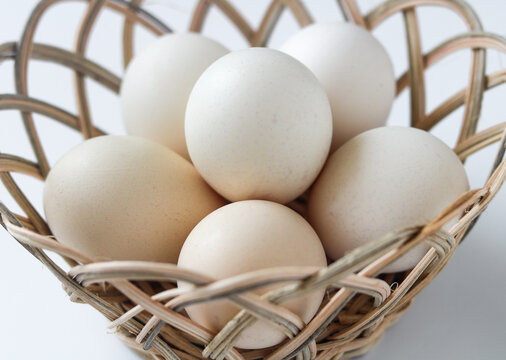 Fresh whole raw eggs arranged neatly inside a woven wooden wicker basket on a white background.