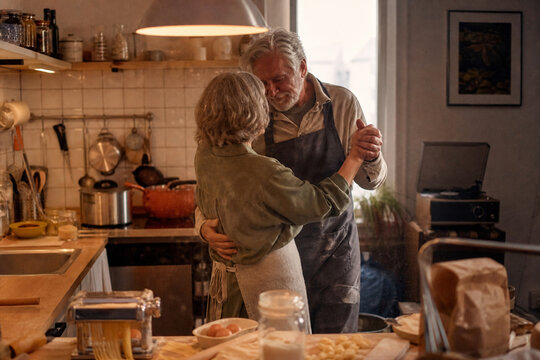 Elderly couple dancing romantically in a cozy kitchen.