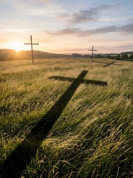 Two crosses stand in a grassy field at sunrise casting long shadows.