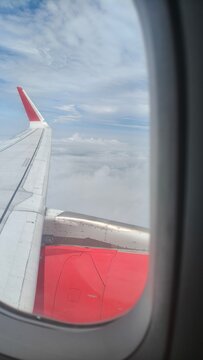 Airplane wing flying high above soft white clouds