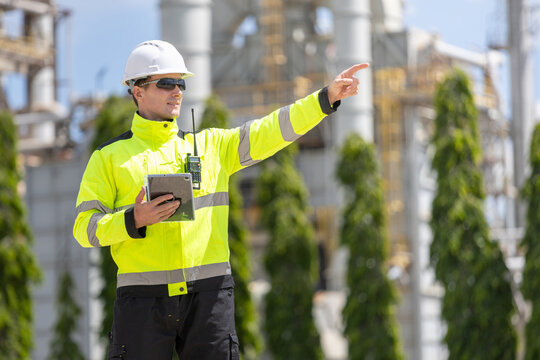 Oil refinery engineer pointing and giving instructions at plant, petroleum plant worker holding digital tablet and walkie talkie, energy industry professional inspecting oil refinery facility outdoors