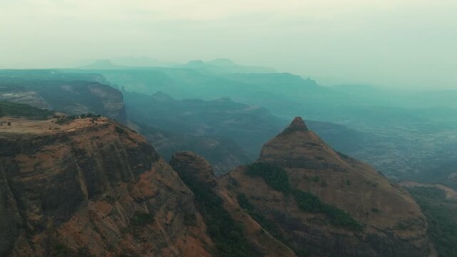Basalt Rock Mountain peaks of the Western Ghats rise through atmospheric haze during early morning at Tiger Point in Lonavla, Maharashtra. Slow camera movement reveals layered ridges and valleys.