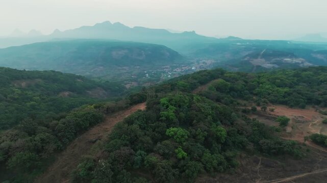 Aerial footage captures forested ridges and mountain ranges in Lonavla, Western Ghats, Maharashtra, India, shrouded in morning mist at sunrise. Slow aerial tracking shot reveals layered terrain.