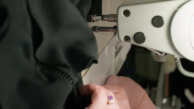 Vertical video. Tailor workshop. Textile craft. Female hand sewing black clothes on stitching machine. Making thread seam on fabric occupation.
