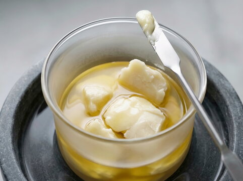 Clarified butter melting in glass container with metal spatula, gourmet cooking ingredient and beauty product base.