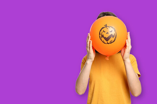 Halloween. Child holds up balloon with pumpkin face, celebrating Halloween festivities