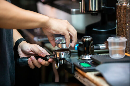 Selective focus to barista putting a dosing funnel onto a portafilter to neatly fill ground coffee powder at a cafe counter before tamping.