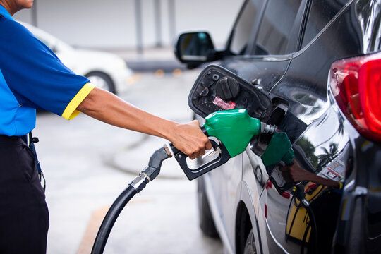 Close-up of a gas station attendant holding a green fuel nozzle to refuel a black car at a petrol station during daytime.