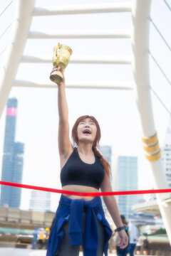 A beautiful, fit woman holds a victory trophy in the middle of the city; a concept promoting health.