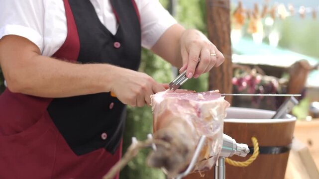 Professional chef slicing authentic prosciutto ham from whole leg on stand during outdoor event.