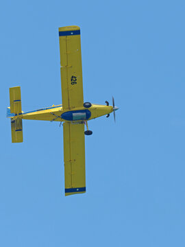 Yellow Propeller Plane Flying Vertically Against a Clear Blue Sky
