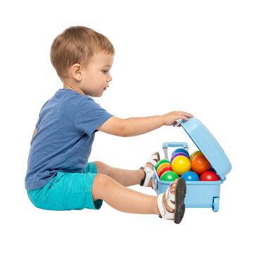Toddler boy opening colorful toy suitcase with balls isolated