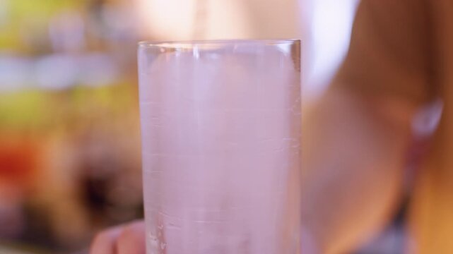 Cocktail making. Stirring ice. Bartender rotating frozen cube in tall glass with spoon on pub counter. Cooling for refreshing drink.