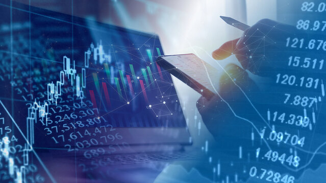 Online stock trading and financial market investment analysis concept. Close-up of businessman hand holding smartphone and pen near laptop computer overlaying digital candlestick graph and financial