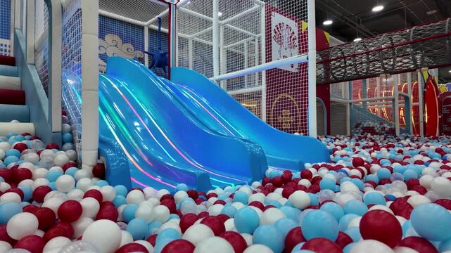 Colorful indoor playground for children featuring blue slides and a large ball pit with plastic balls.