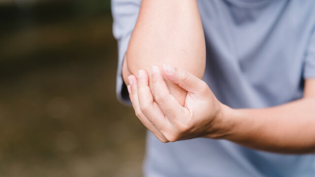 Close up of an unrecognizable man holding his painful elbow outdoors. Concept of tennis elbow, joint inflammation, physical sports injury, arthritis, and the need for medical healthcare.
