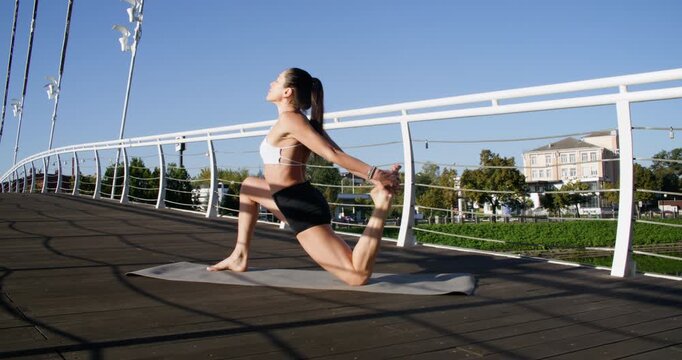 Yoga practice. Outdoor workout. Sportive woman doing physical stretching exercise performing athletic pose on bridge in park.