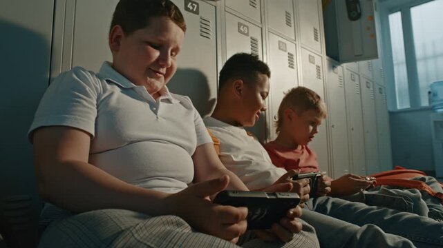 Generation Alpha Students Spending Free Time Together in School Hallway, Sharing Entertainment on Digital Devices while Relaxing Near Lockers. Friendship, Diversity, Education, Connected Childhood.