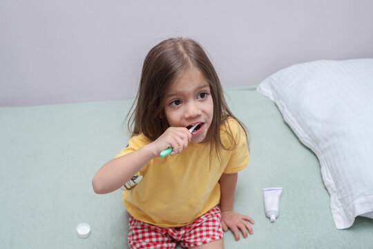Young Girl Brushing Teeth With Toothbrush While Sitting On Sofa In Bright Home Interior, Showing Daily Oral Care Routine, Childhood Hygiene, Healthy Smile Habits, Relaxed Indoor Scene,