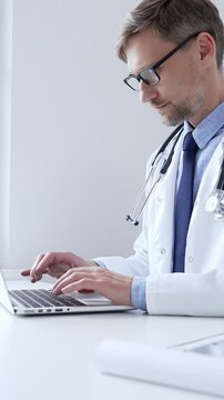 Middle aged doctor man is diligently typing on a laptop, likely updating patient records or conducting research, showcasing the intersection of healthcare and technology in medical setting. Medicine