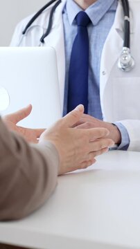 Male doctor is taking notes with laptop while listening to a female patient explaining her symptoms during a medical consultation in the clinic office. Medicine and health care