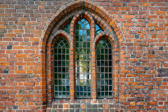 Window with vintage glass panes. Window in traditional European brick architecture. Historic Gothic window on old exterior. Medieval church window with pointed arches.