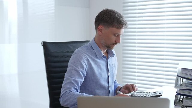 Male professional accountant calculating invoices and managing bills while reviewing financial reports in an office setting. Audit and taxes theme in business