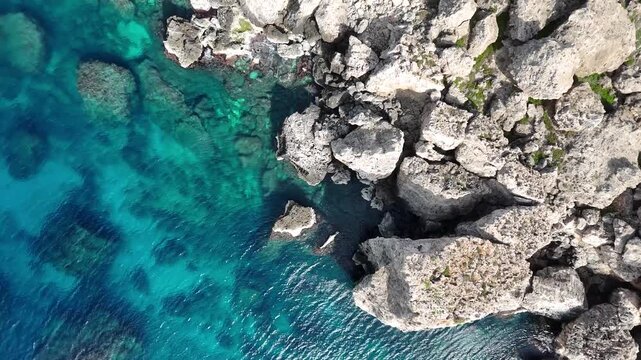 limestone rocks jagged coastline malta turquoise water reef patterns visible clear sea birds eye drone shot rugged texture erosion coastal mediterranean