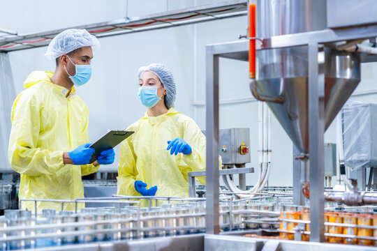 Food canning factory quality control inspectors checking production line, factory workers in protective suits with clipboard discussing production process and inspecting canned food