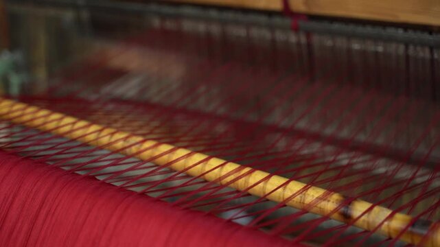 Close up of traditional loom weaving red fabric in slow motion at artisanal textile workshop.