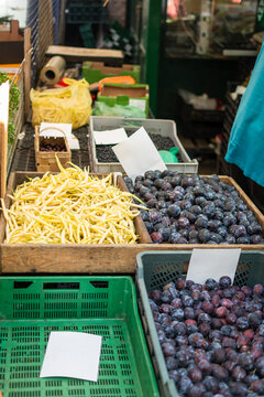 Vertical photo of yellow beans and plums on a bench at an outdoor local market.