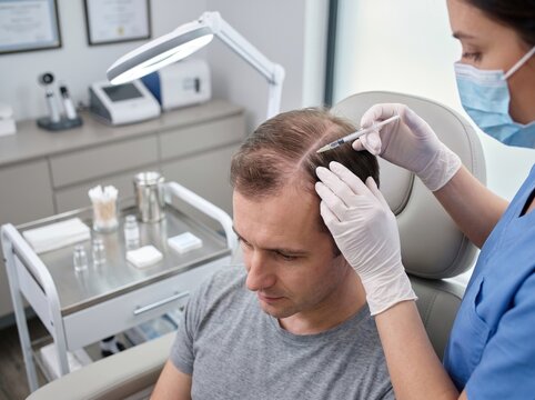 A man reclines as a gloved specialist injects mesotherapy solution into his scalp, a hair restoration and hair growth treatment concept.