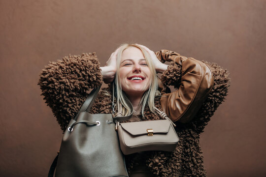 A stylish blonde woman wearing a teddy coat paired with vintage bags, standing against a rich brown background in shade Mocha Mousse