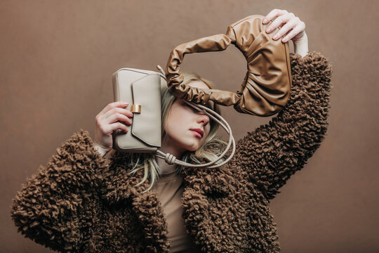 A stylish blonde woman wearing a teddy coat paired with vintage bags, standing against a rich brown background in shade Mocha Mousse