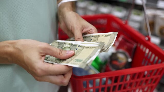 Close up view of woman hands counting cash money Indian rupee banknotes for shopping in supermarket. Red basket in background. Calculating budget to spend in grocery store. Financial planning concept.