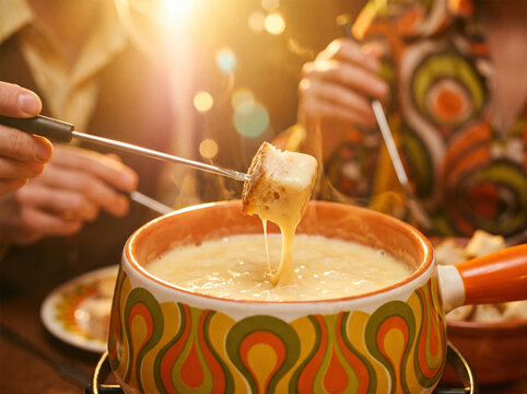 Bread cube dipped in melted Swiss cheese fondue bubbling in retro ceramic caquelon pot