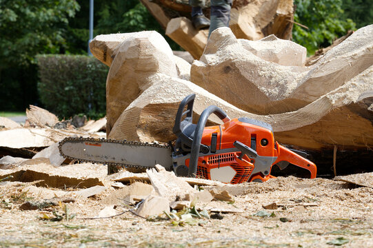 Orange Chainsaw Resting on Wood Chips After Tree Carving Activity in Outdoor Park Setting